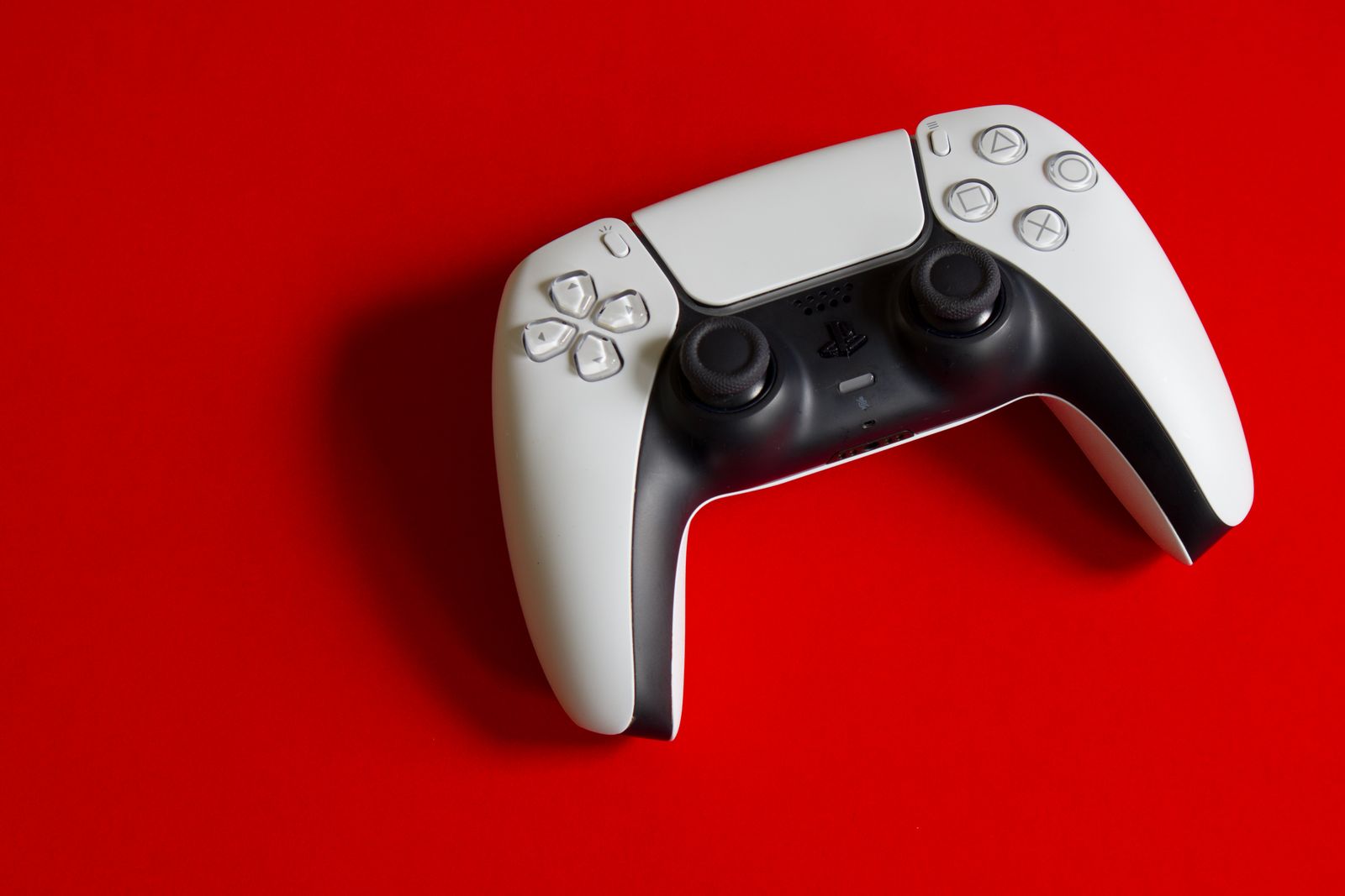 White DualSense controller on a red studio backdrop.